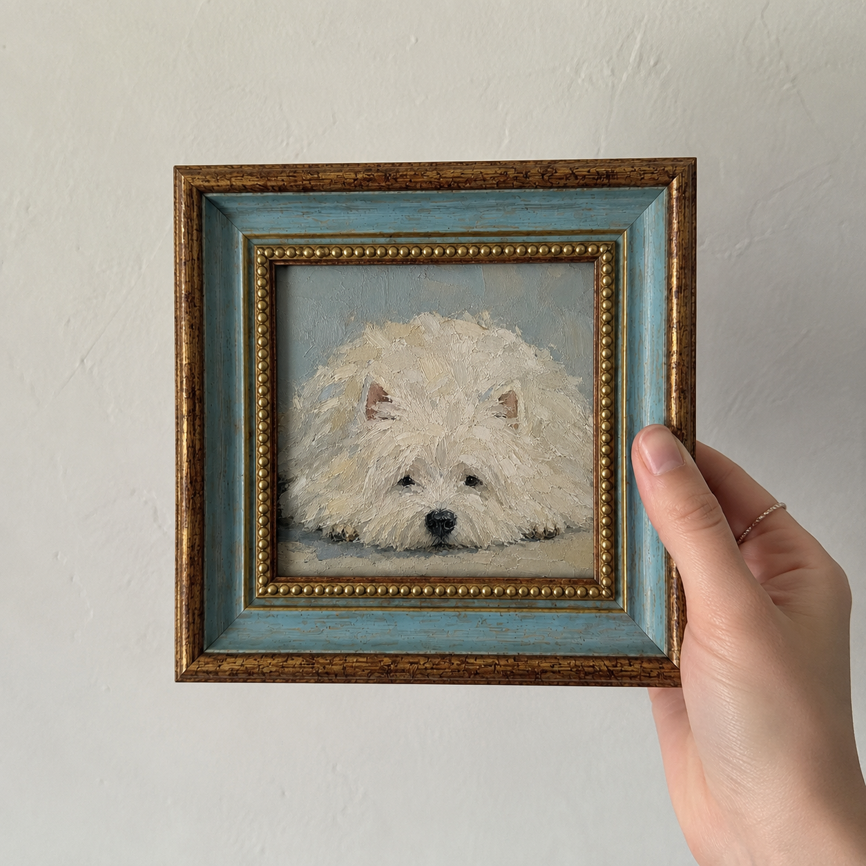 Framed oil painting of a fluffy West Highland white terrier resting with its head on the floor, held in a hand.