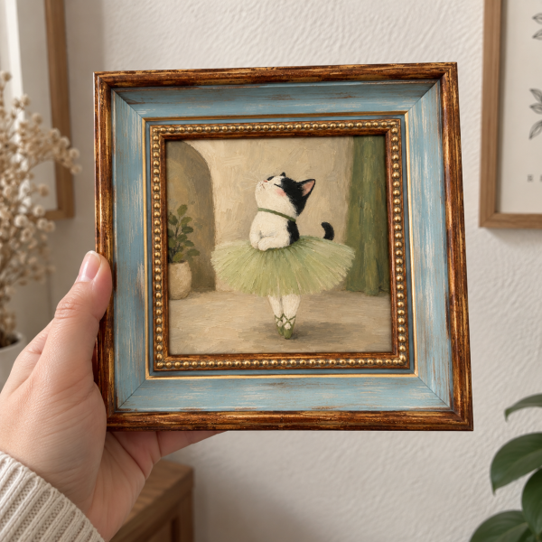 Framed oil painting of a tuxedo cat dressed as a ballerina, held in a hand.