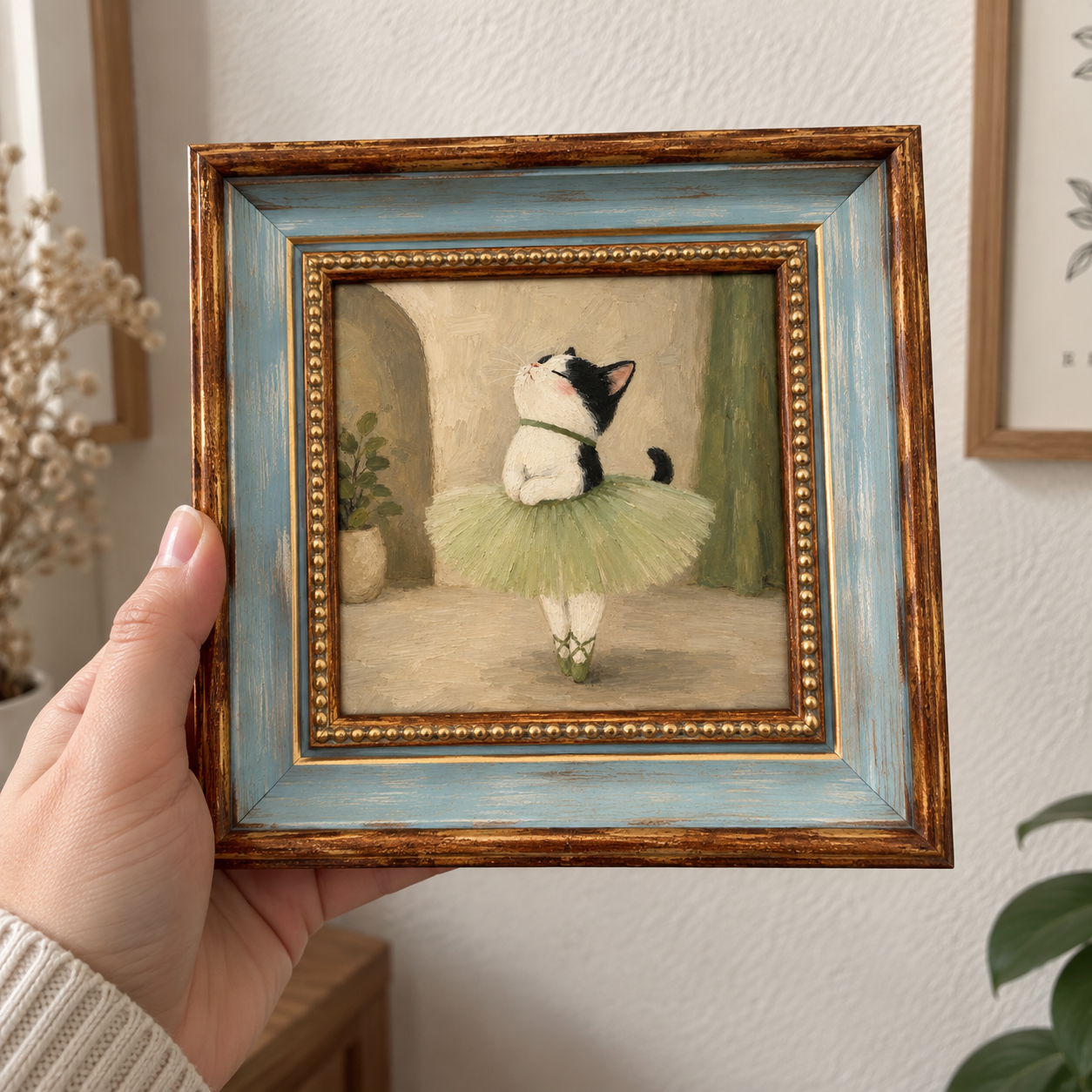 Framed oil painting of a tuxedo cat dressed as a ballerina, held in a hand.